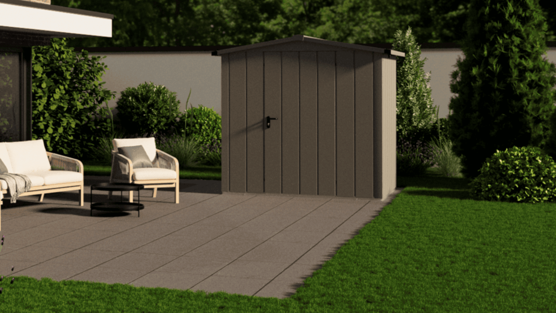 A small brown garden shed with a black door handle stands on a tiled patio, next to two outdoor chairs and a small table, surrounded by green grass, shrubs, and trees.
