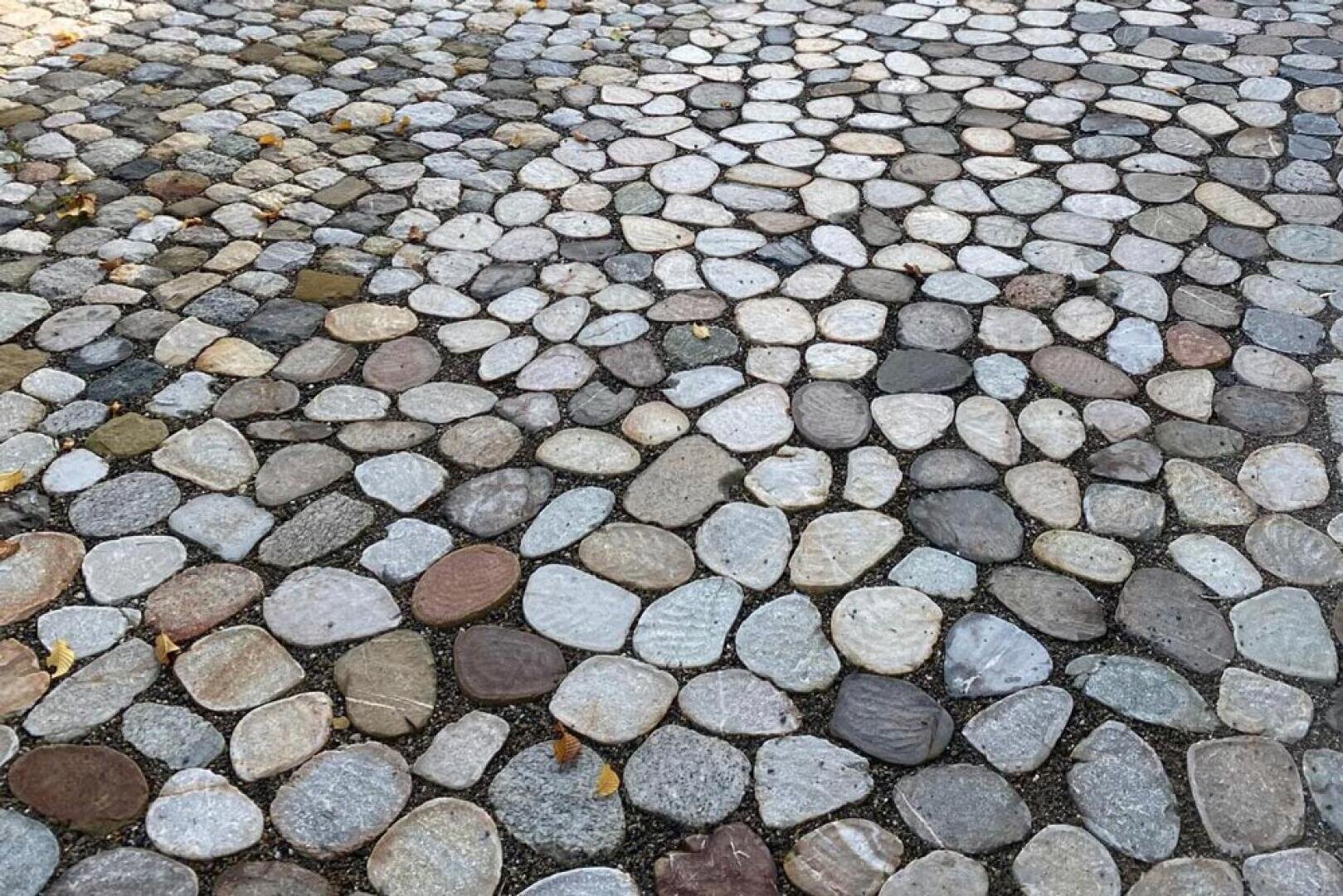 Nahaufnahme eines Steinpflasters aus flachen Steinen unterschiedlicher Form und Größe, die in einem kreisförmigen, mosaikartigen Muster angeordnet sind, wobei einige Blätter zwischen den Steinen verstreut sind.
