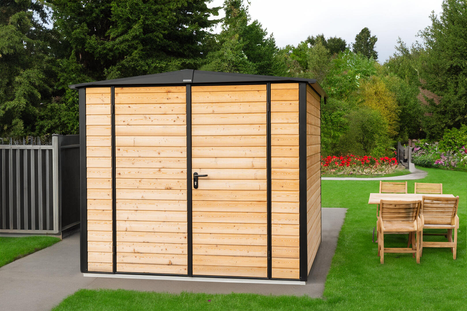 Ein hölzernes Gartenhaus mit schwarzem Rahmen und einer verschlossenen Tür steht auf einer gepflasterten Fläche neben einer Rasenfläche mit einem hölzernen Esstisch und Stühlen; im Hintergrund stehen Bäume und bunte Blumenbeete.