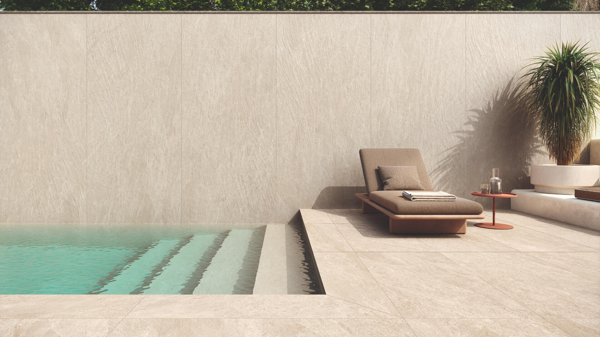 Eine moderne Außenterrasse mit einem Swimmingpool, einem gepolsterten Liegestuhl mit gefalteten Handtüchern, einem kleinen roten Beistelltisch mit einem Glas und einer Karaffe sowie einer hohen Topfpflanze an einer beigen Steinmauer.