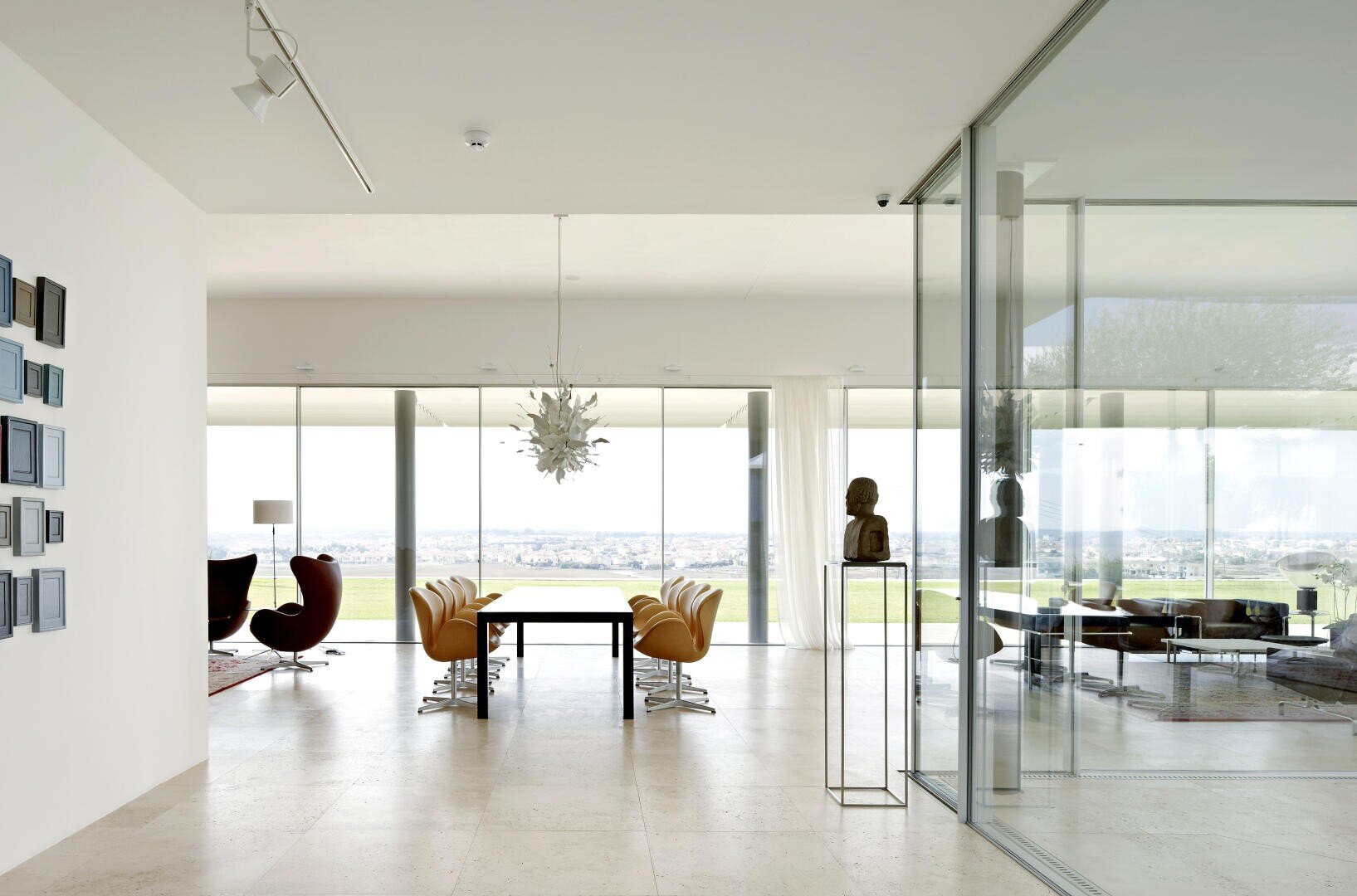 Modern dining room with a long table, yellow chairs and a sculptural chandelier, with floor-to-ceiling windows, glass walls and views of a green landscape and the city skyline in the distance.