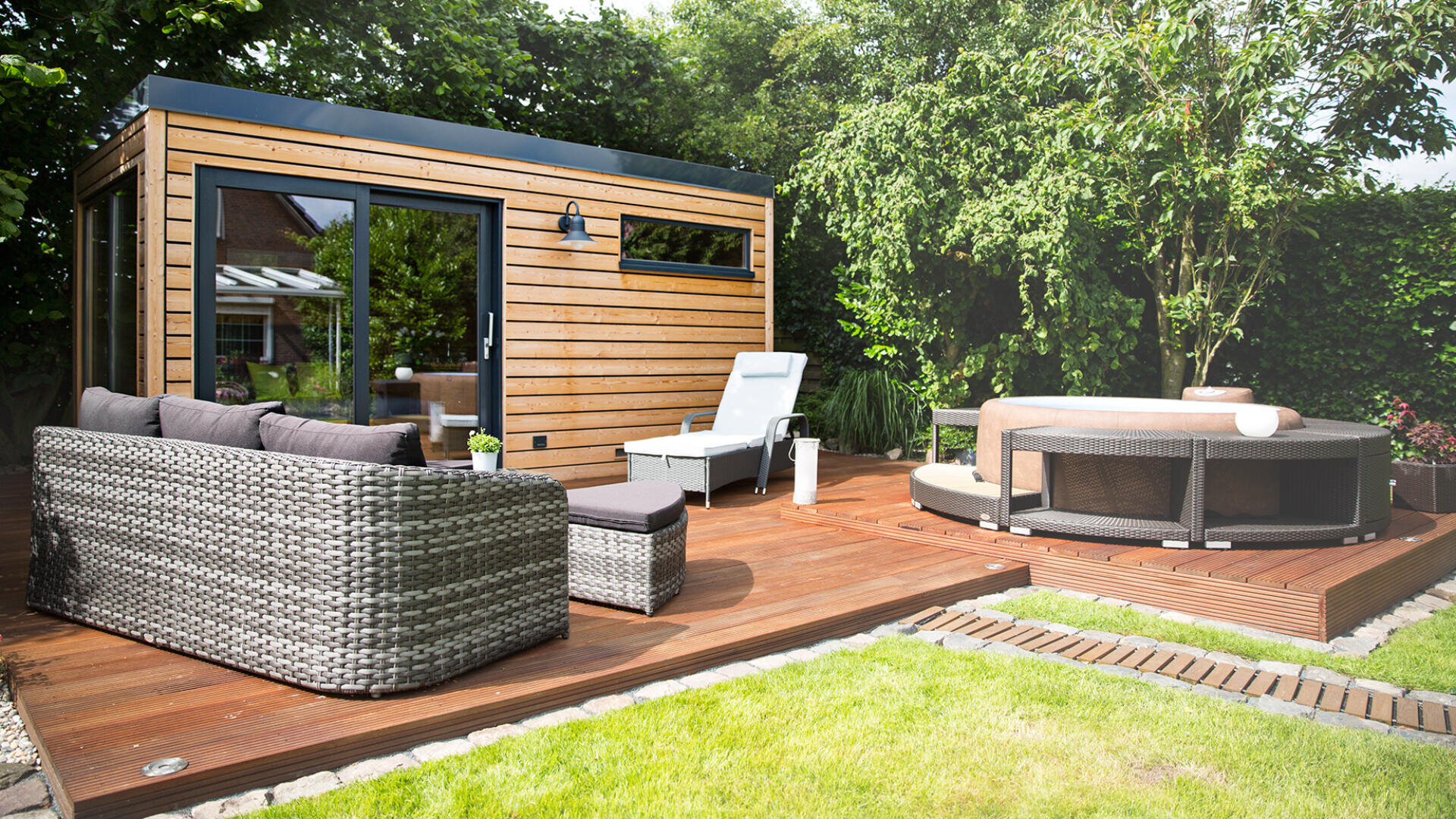 Der moderne Hinterhof verfügt über eine Holzterrasse mit einem runden Whirlpool, Rattansofas und -stühlen und einem kleinen, stilvollen Gartenhaus aus Holz, umgeben von viel Grün und einem gepflegten Rasen.