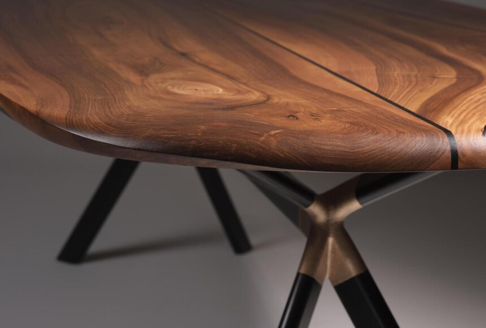 Nahaufnahme eines Holztisches mit glatter, polierter Oberfläche und natürlicher Holzmaserung, der von schwarzen Metallbeinen mit einzigartigem Gelenkdesign getragen wird.