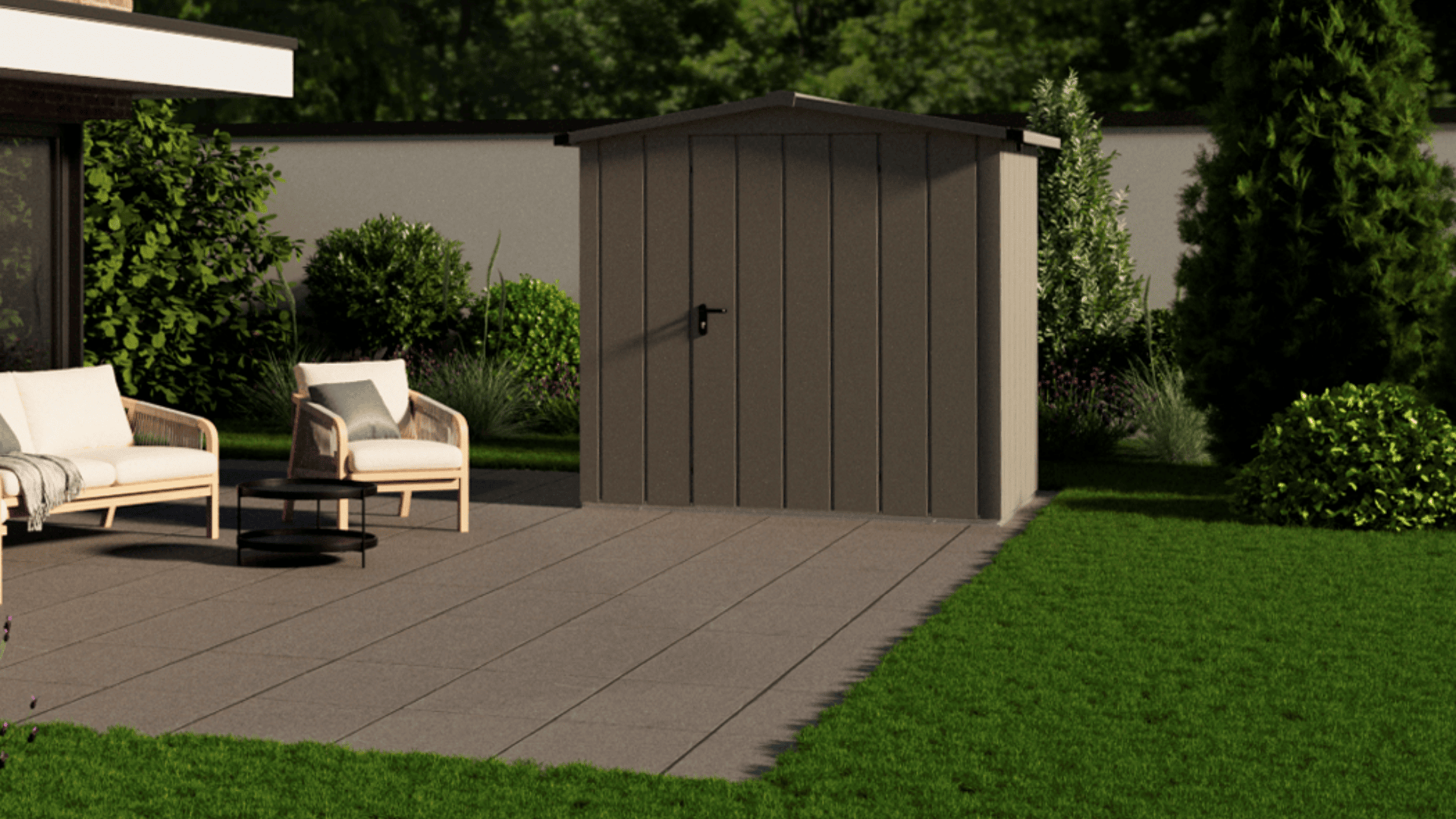 Ein kleines braunes Gartenhäuschen steht auf einer gefliesten Terrasse neben Gartenstühlen und einem Tisch, umgeben von grünem Gras, Sträuchern und Bäumen, mit einer weißen Mauer im Hintergrund.