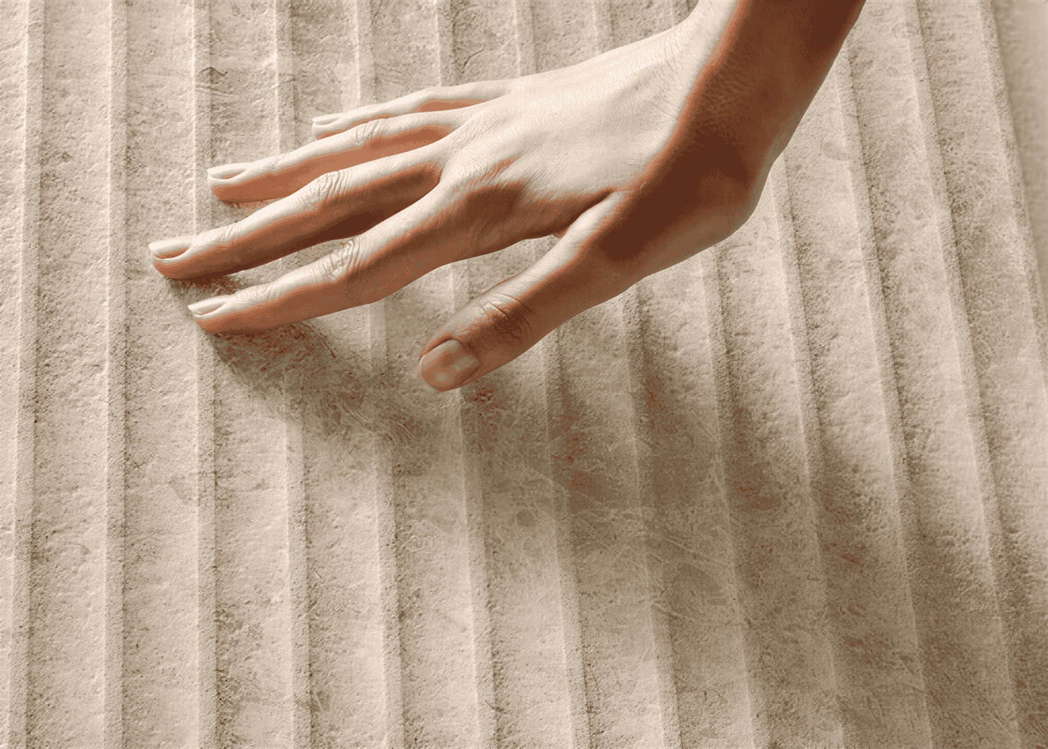 Eine Hand berührt sanft eine strukturierte, gerippte Oberfläche, möglicherweise Stoff oder Pappe, wobei eine sanfte Beleuchtung die Textur und Konturen hervorhebt.