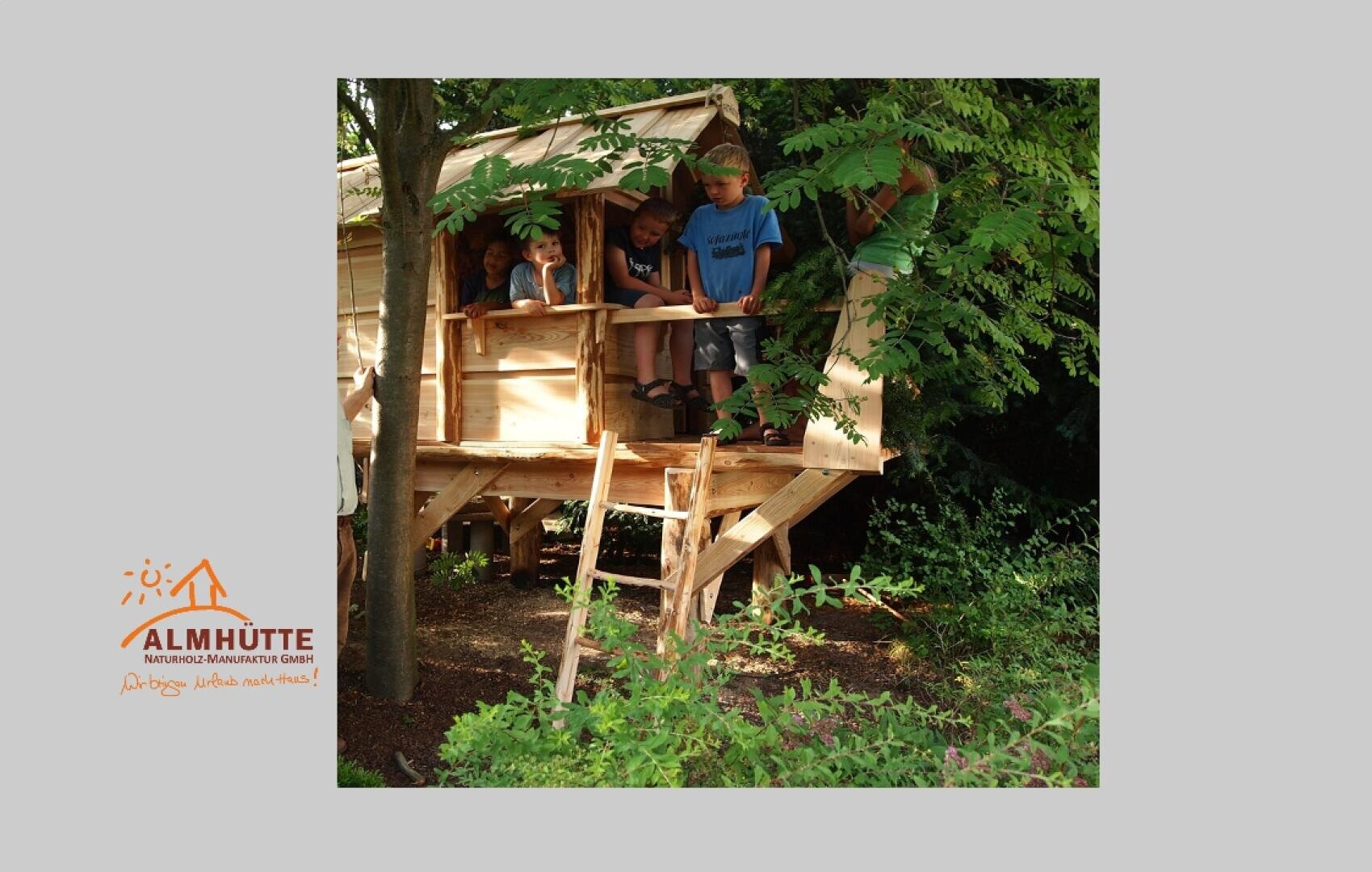 Mehrere Kinder stehen und lehnen sich über das Geländer eines hölzernen Baumhauses, das von üppig grünen Bäumen umgeben ist. Das Sonnenlicht dringt durch die Blätter, und in der unteren linken Ecke erscheint ein Logo der Almhütte.