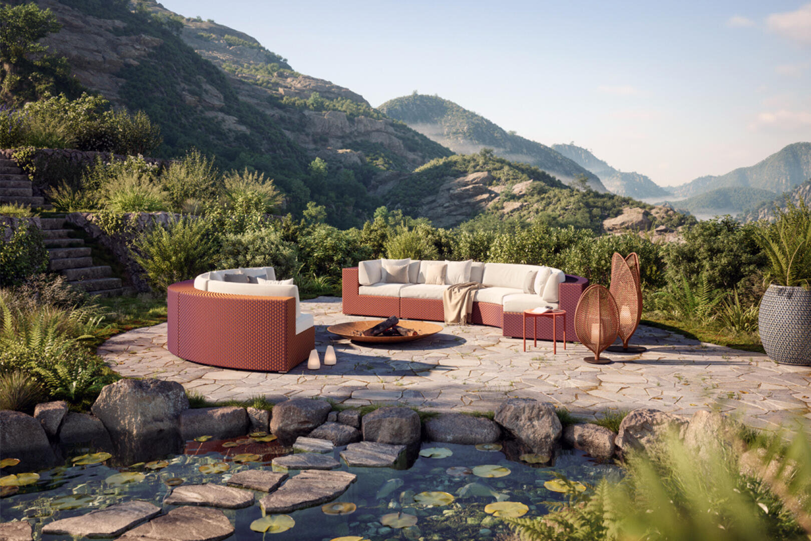 Curved outdoor seating with cushions surrounds a fire pit on a stone patio, set in a lush, mountainous landscape with greenery and a pond featuring lily pads and rocks in the foreground.