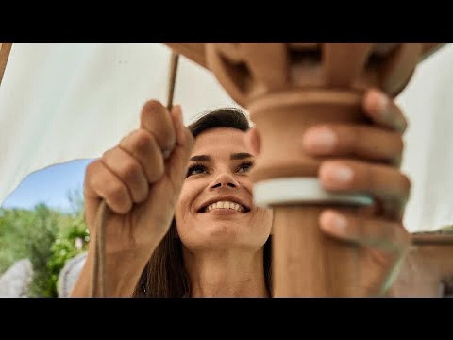 Eine Frau lächelt, während sie im Freien mit ihren Händen an einem Terrakotta-Objekt arbeitet und sich ganz auf ihre Aufgabe konzentriert.