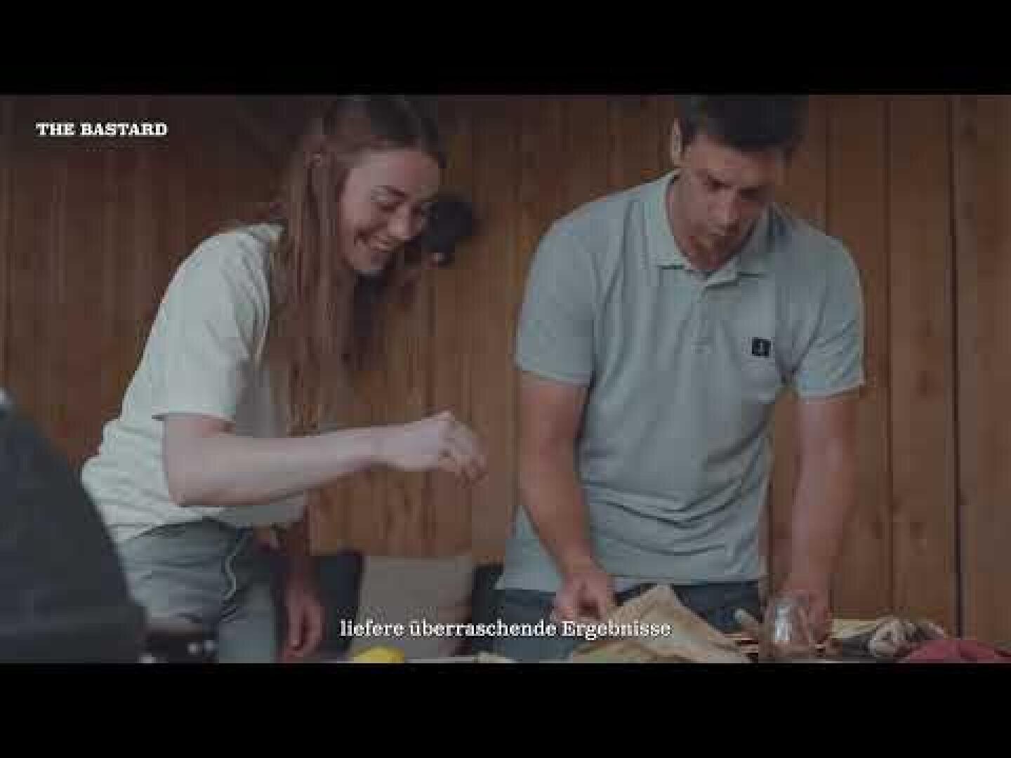 Eine Frau und ein Mann stehen lächelnd an einem Holztisch und bereiten in einem Innenraum gemeinsam Essen zu. Der Text auf dem Bild lautet THE BASTARD und liefere überraschende Ergebnisse.