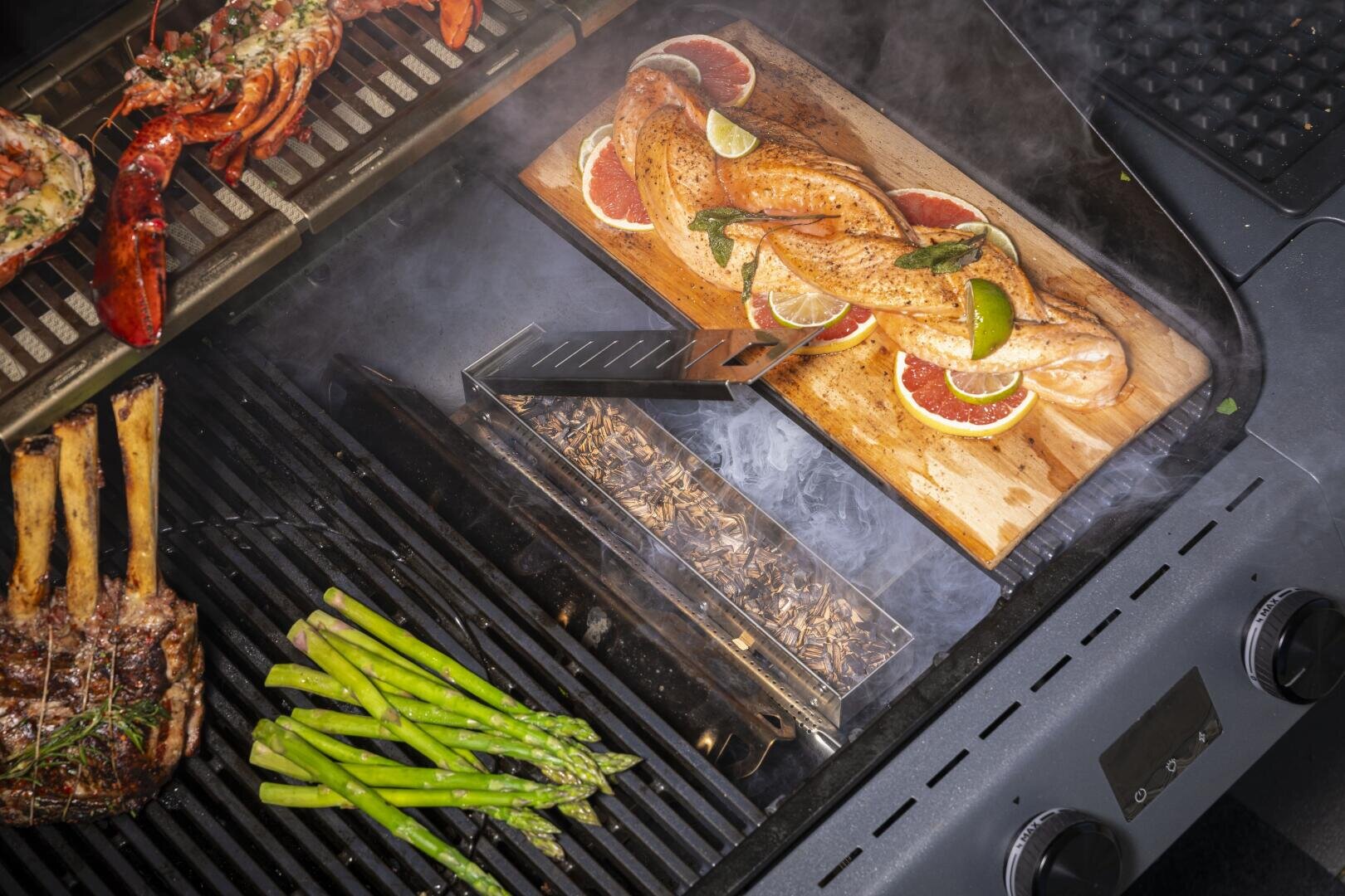 Grillen Sie geräucherten Lachs auf einer Zedernholzplanke mit Limette und Kräutern, Hummerschwänze, Spargel und ein Lammkarree; eine Räucherbox mit Holzspänen sorgt für zusätzlichen Geschmack.
