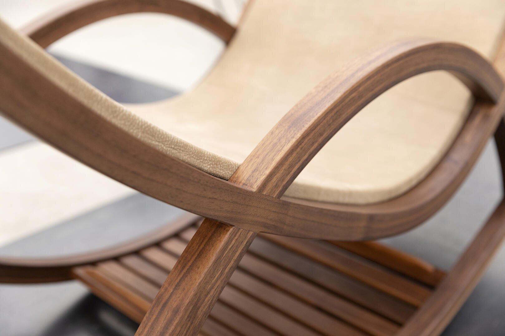Nahaufnahme eines modernen Schaukelstuhls mit glatten, geschwungenen Holzarmen und einem beigen Stoffsitz, der die elegante Handwerkskunst und die natürliche Holzmaserung zur Geltung bringt.