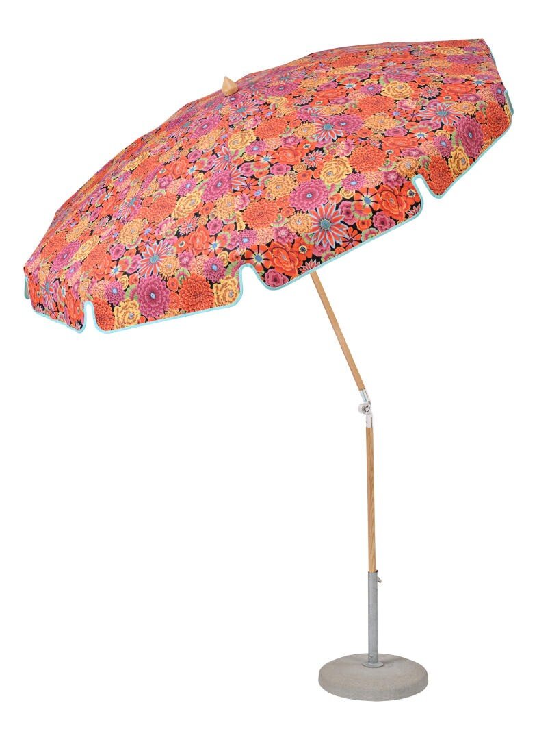 A large outdoor umbrella with a wooden pole and a vibrant, floral-patterned fabric canopy in shades of red, orange, and pink, standing in a round gray base.