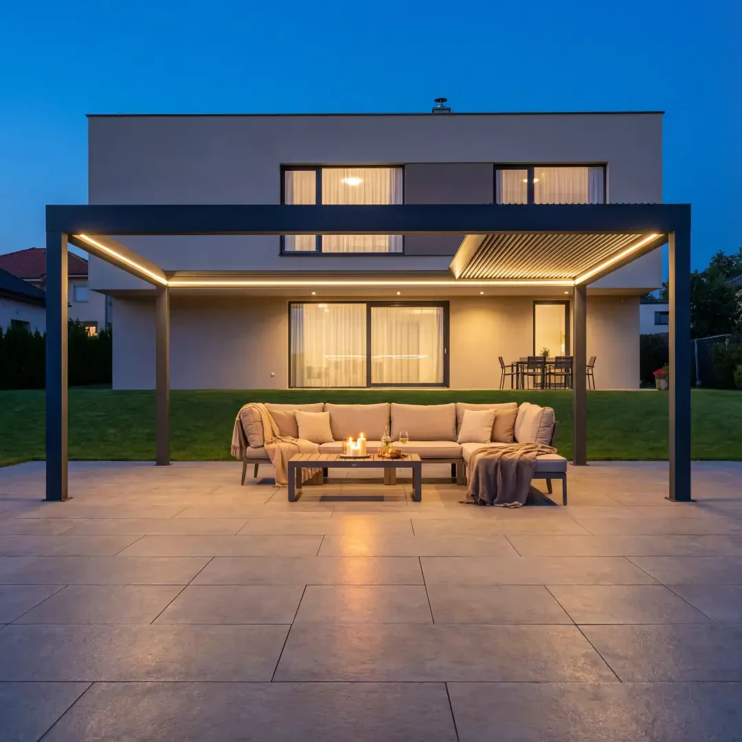 Ein moderner Hinterhof in der Abenddämmerung mit einer Pergola mit sanfter Beleuchtung, einem großen beigen Sofa im Freien, einem Couchtisch mit Kerzen und einem modernen zweistöckigen Haus im Hintergrund.