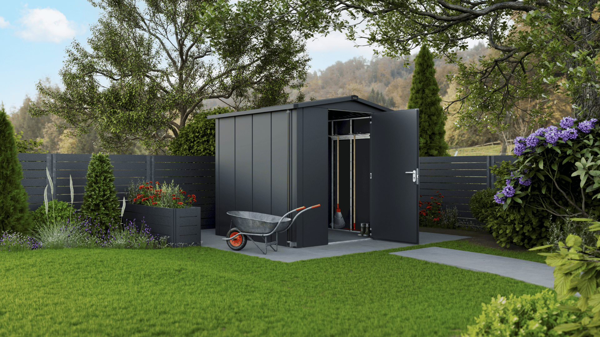 Ein modernes graues Metall-Gartenhaus steht offen auf einer gepflasterten Fläche, umgeben von üppigem grünen Gras, Bäumen, Blumen und einem schwarzen Zaun. Eine Schubkarre und einige Gartengeräte sind vor dem Schuppen zu sehen.