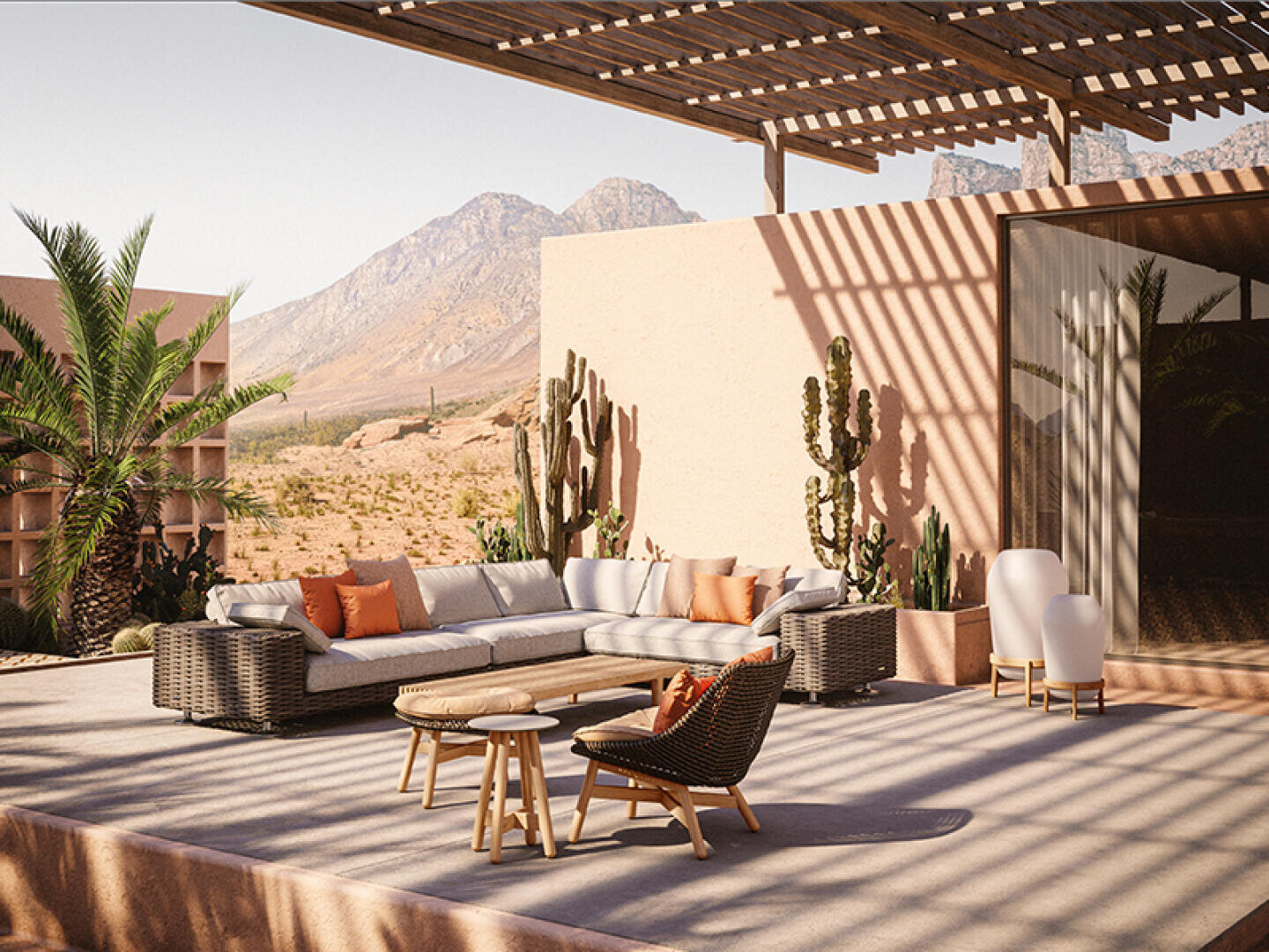 Modern outdoor patio with a large sectional sofa, chairs, and small tables, set under a wooden pergola. Desert plants, including cacti and palm, surround the space; mountains and blue sky are visible in the background.