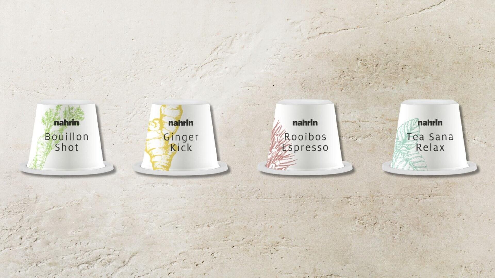 Four white Nahrin beverage pods are lined up against a light stone background. The pods are labeled Bouillon Shot, Ginger Kick, Rooibos Espresso, and Tea Sana Relax, each with a colored design.