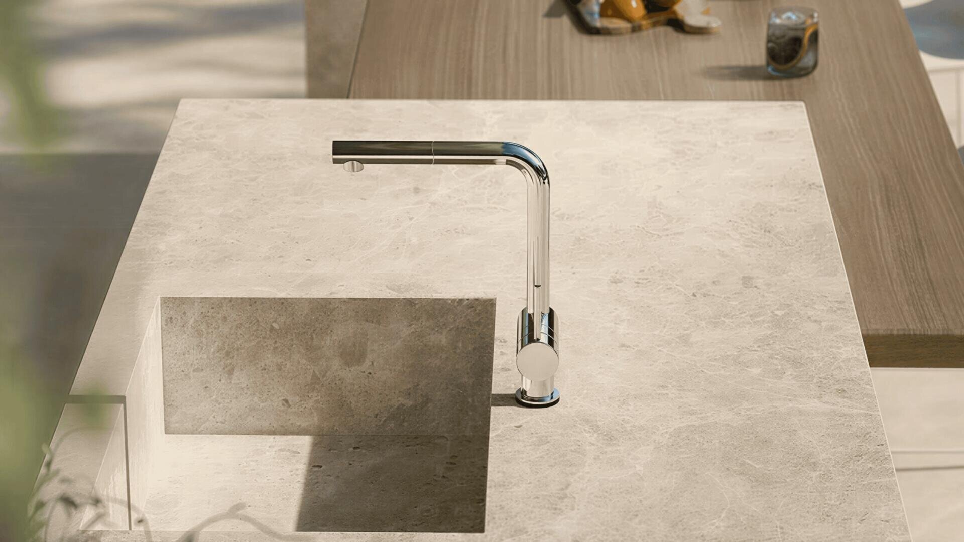 Die moderne, verchromte Küchenarmatur in minimalistischem Design ist auf einer Arbeitsplatte aus hellbeigem Stein mit integrierter rechteckiger Spüle in einer modernen Küche montiert.