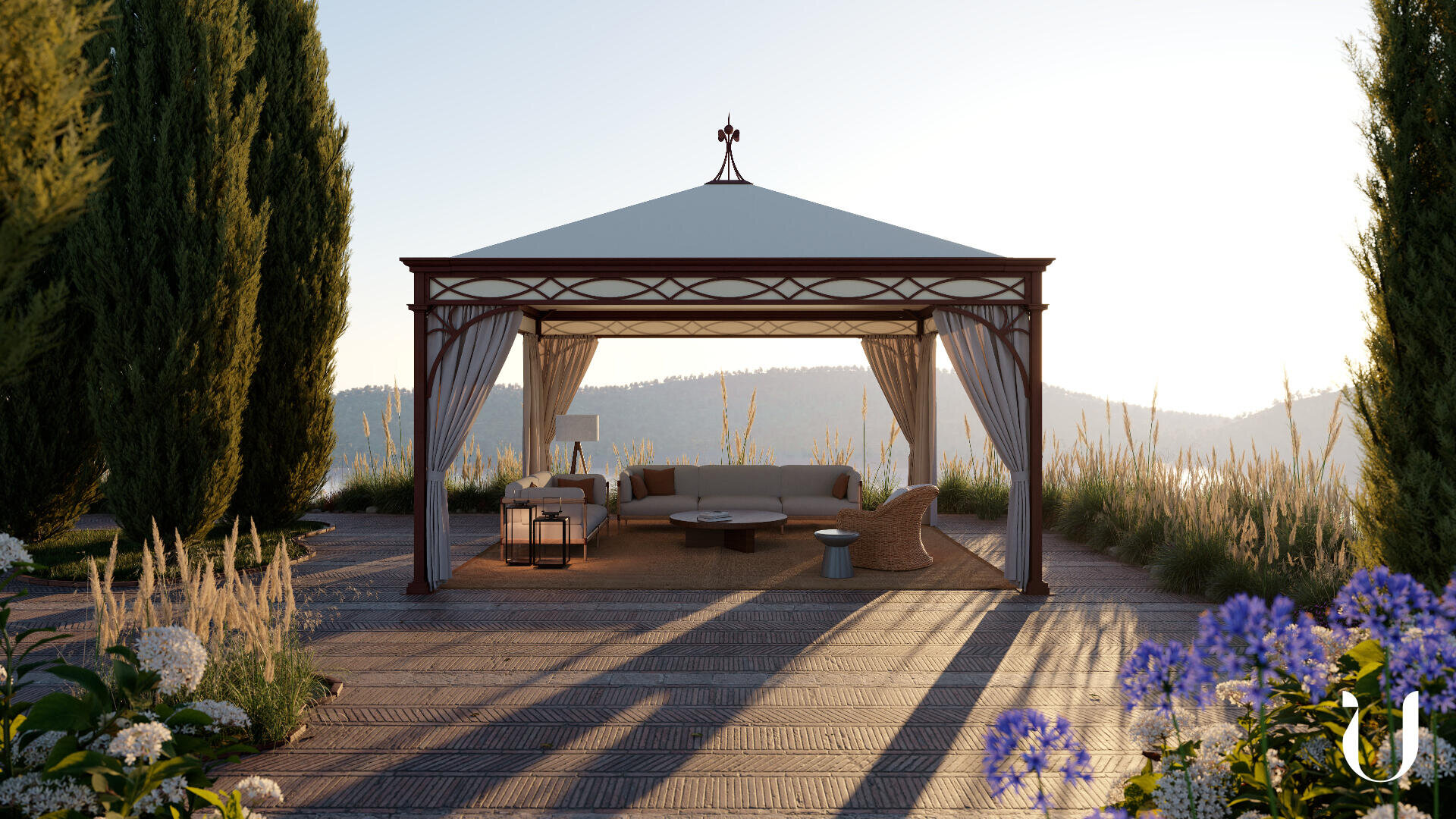 Ein Pavillon mit weißen Vorhängen steht auf einer gepflasterten Fläche, umgeben von hohem Gras, Bäumen und Blumen. Im Inneren befinden sich Sofas, ein Couchtisch und Liegestühle, mit den Bergen im Hintergrund bei Sonnenuntergang.