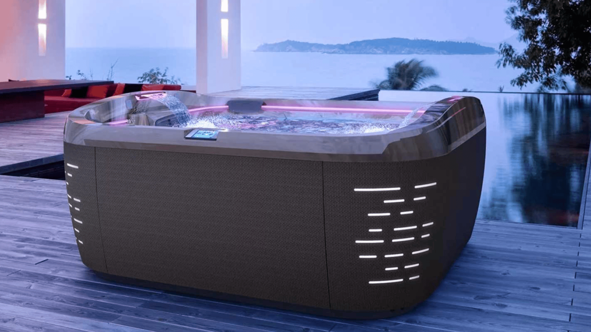 Ein moderner Whirlpool mit LED-Beleuchtung steht auf einer Holzterrasse neben dem Infinity-Pool und bietet in der Abenddämmerung einen herrlichen Blick auf das Meer.