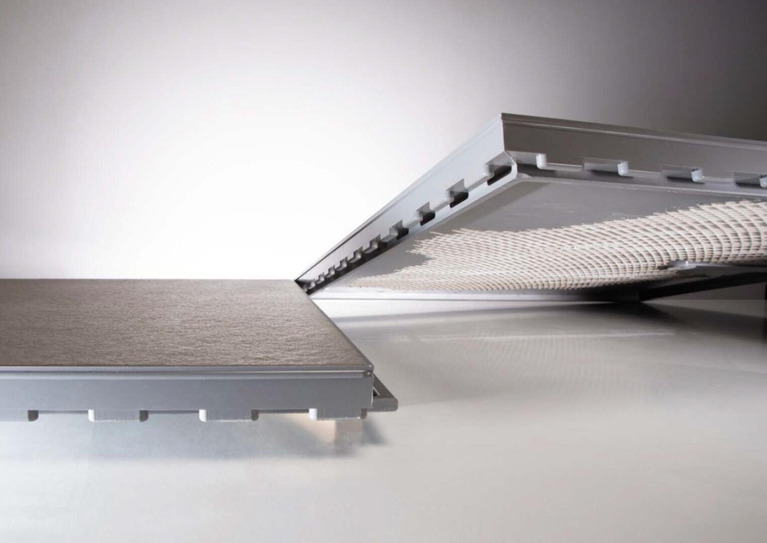 Abgebildet sind zwei rechteckige Platten, von denen eine flach liegt, während die andere aufgeklappt ist und eine gewebte oder netzartige Innenstruktur offenbart. Die Paneele haben einen Metallrahmen und eine strukturierte graue Außenfläche.