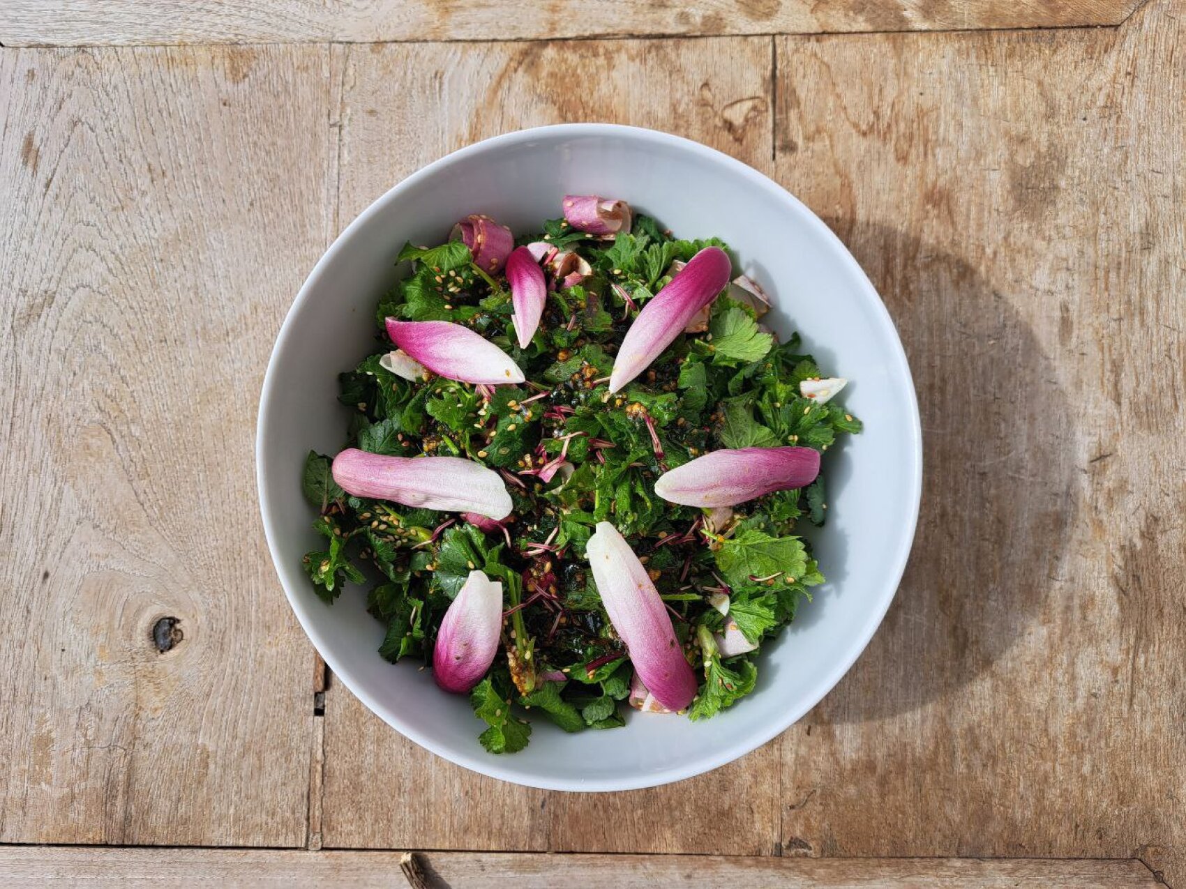 On a rustic wooden table stands a white bowl of green lettuce with purple and white endive leaves.
